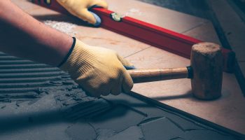 The working tiler knocks on the tile with a Tile Mallet, the professional checks the building level